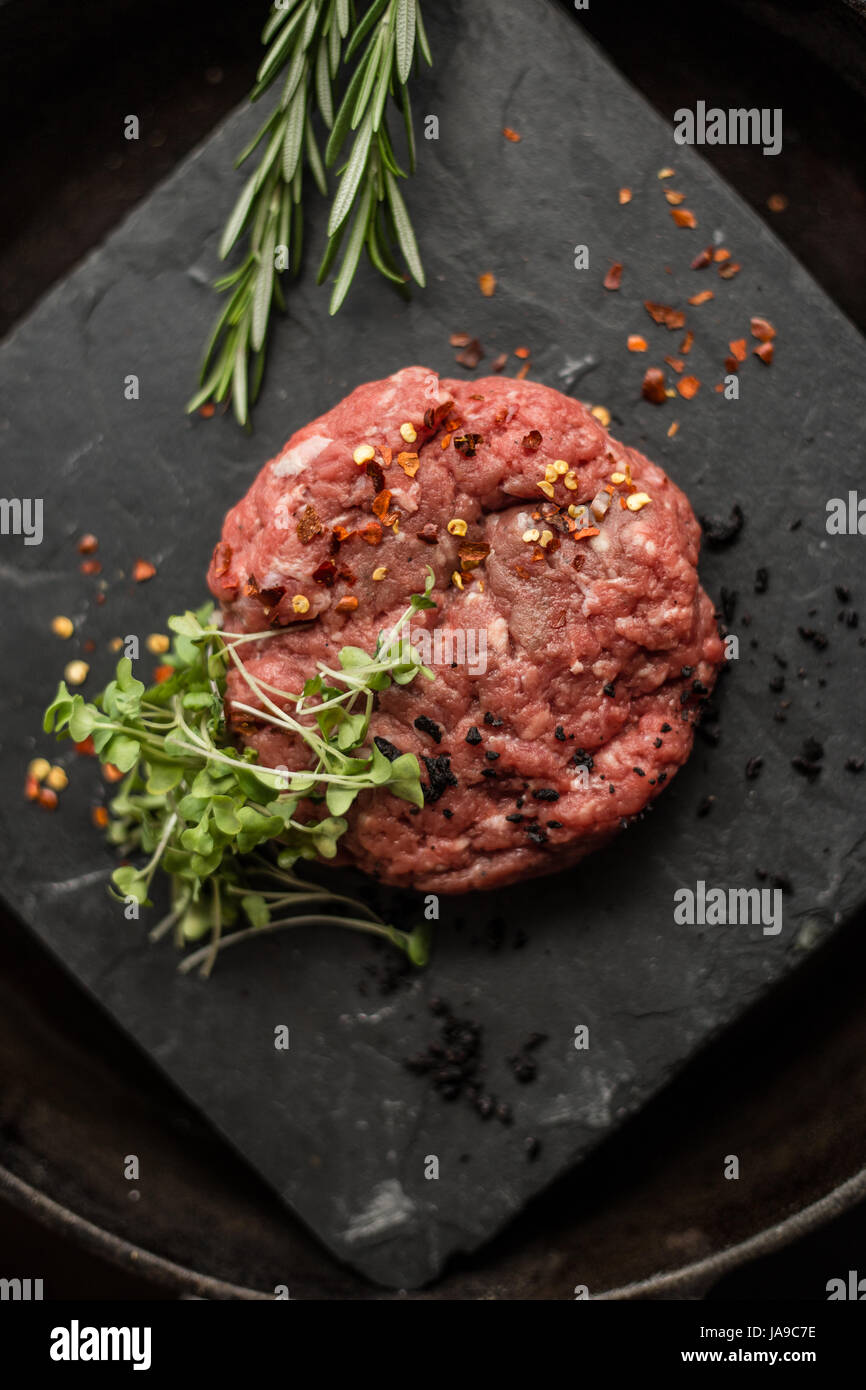 Raw ground beef meat steak cutlets with herbs and spices on black board. Restaurant Stock Photo