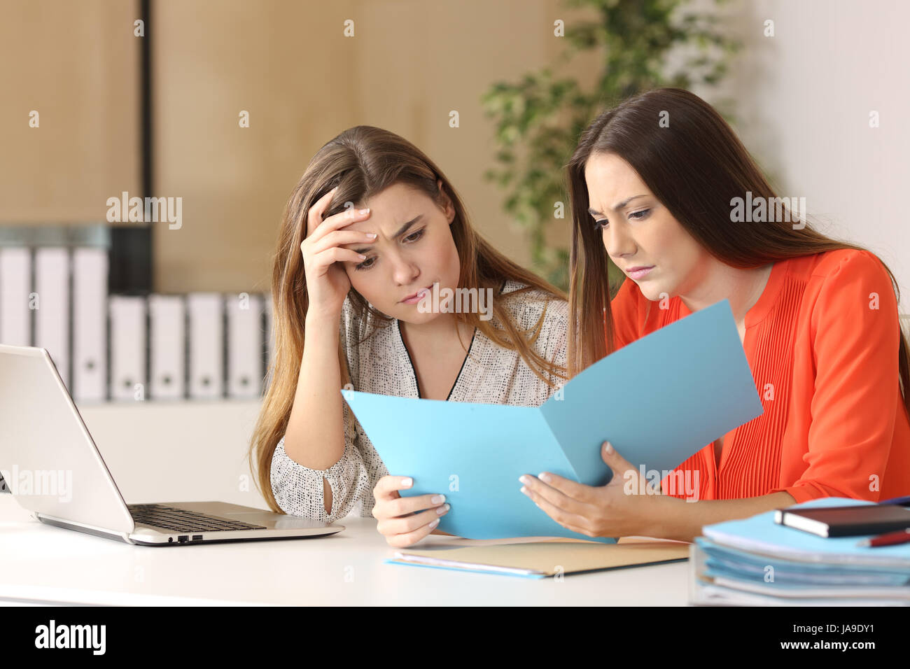 Two worried coworkers reading a report together in a desk at office Stock Photo