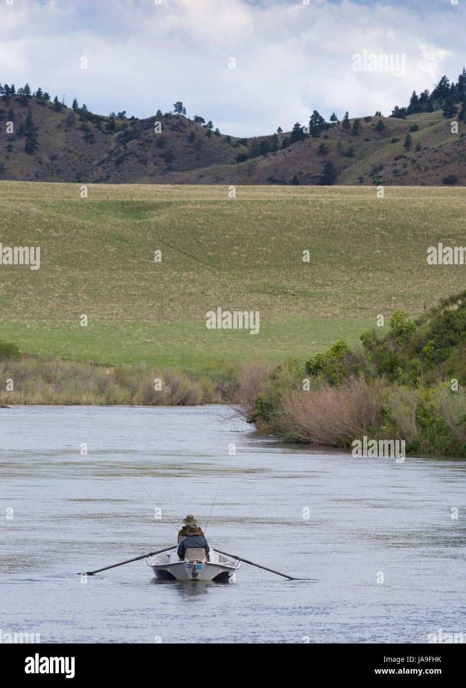Fly fishermen in a boat photographed from behind on the Missouri River with foothills in the background. Foothills and mountains are in background. Stock Photo