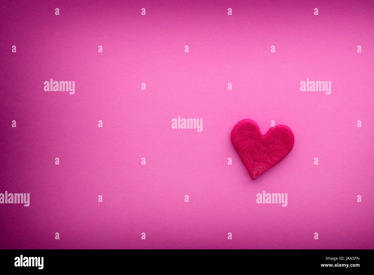 Red heart with small cracks on a pink background with vignette. Close up. Stock Photo