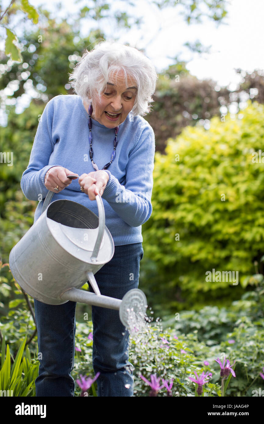 Senior woman watering flowers in garden Stock Photo - Alamy