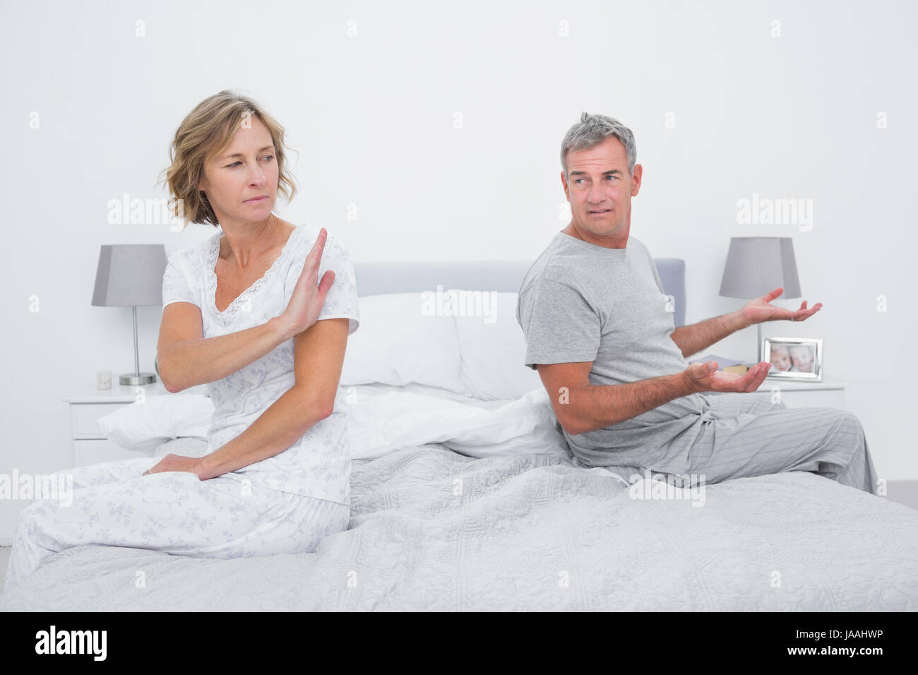 Couple sitting on different sides of bed having an argument in bedroom