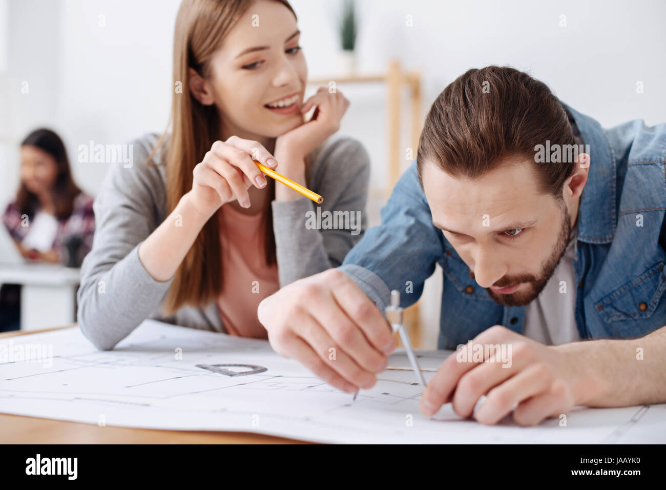 Make it a little wider. Enchanting diligent talented engineer guiding her friend every step of the way as they working on a blueprint of the new build Stock Photo