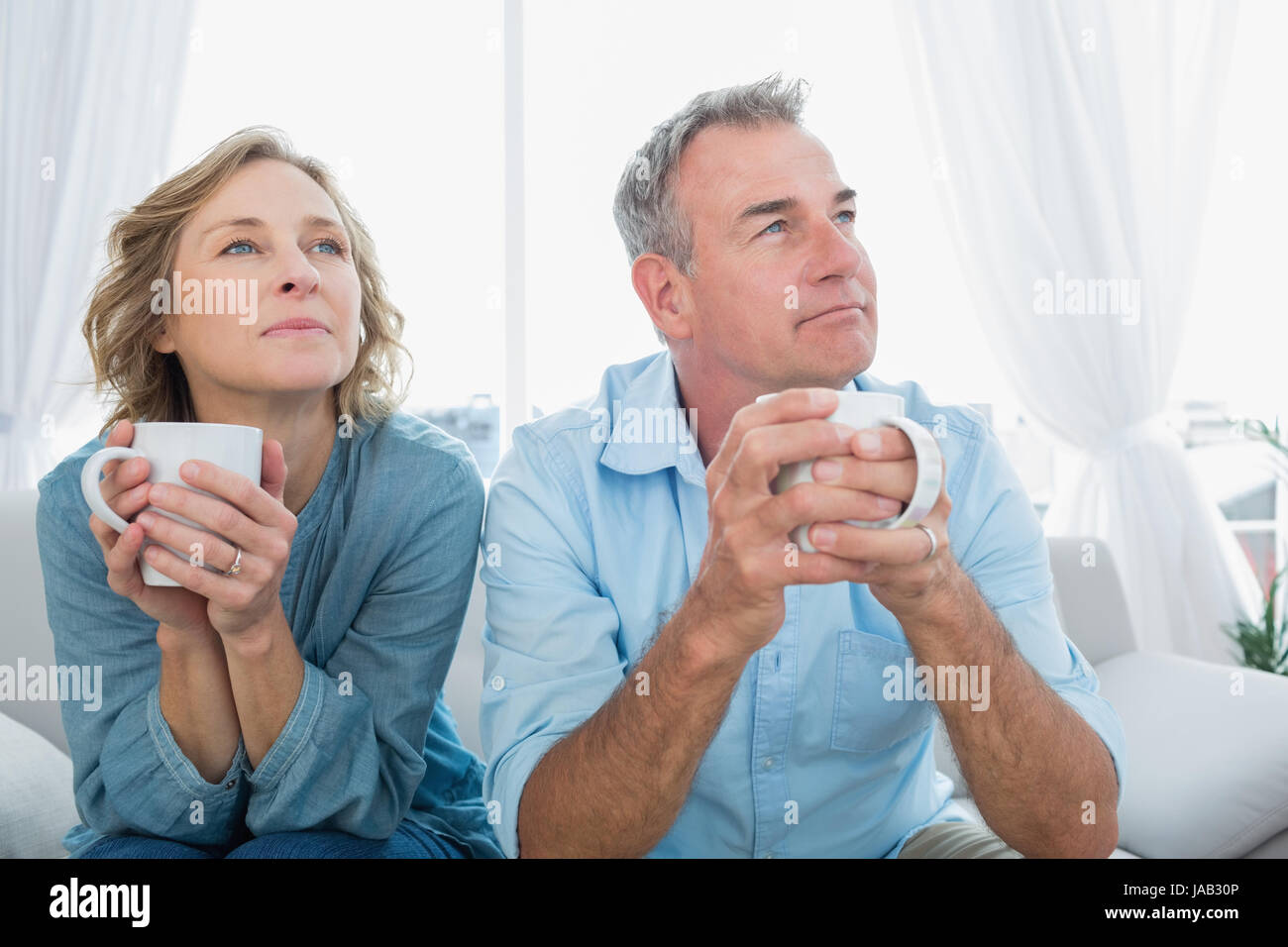 Thoughtful middle aged couple sitting on the couch having coffee ...