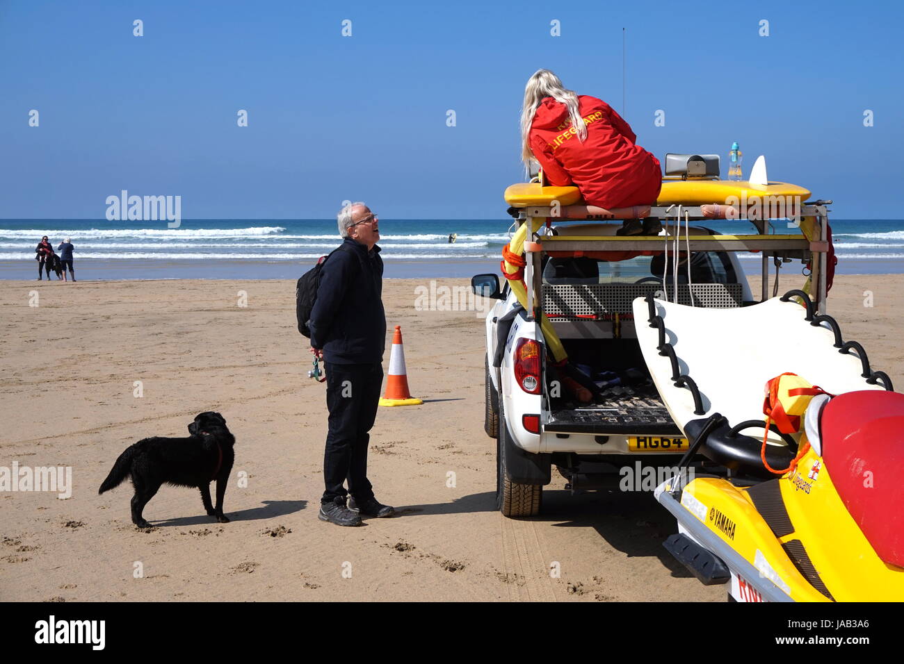 Newquay, Cornwall, UK - April 7 2017: Female RNLI lifeguard talking to a man with a dog on a surfing beach in Newquay Stock Photo