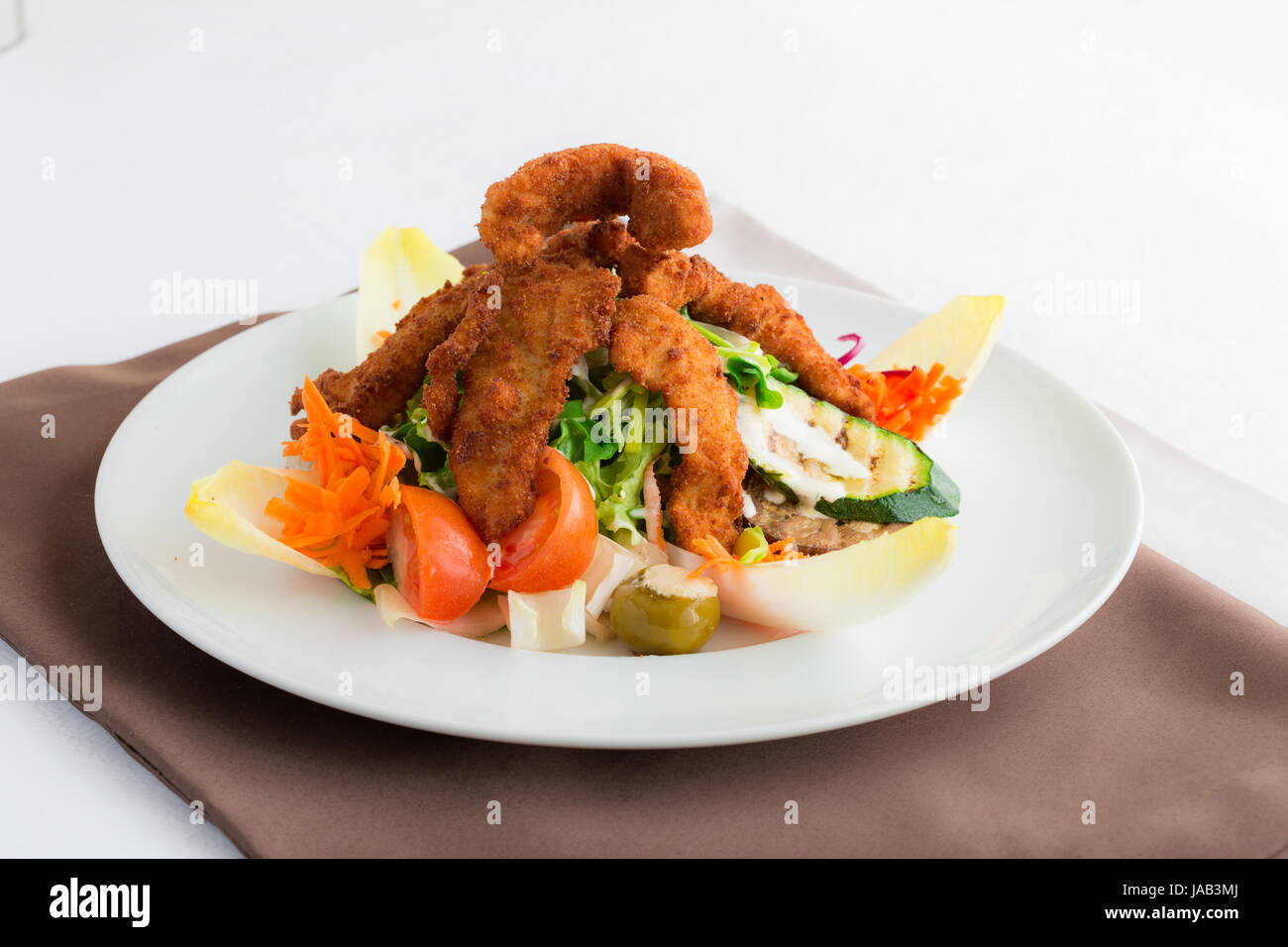 Mixed salad with green salad, endives, tomatoes, courgettes, olives, carrots and fried chicken. This is an Italian recipe. Stock Photo