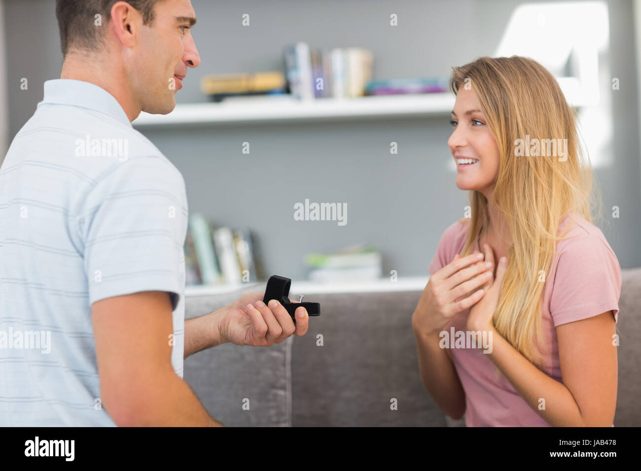 Man on one knee proposing to girlfriend in sitting room at home Stock Photo