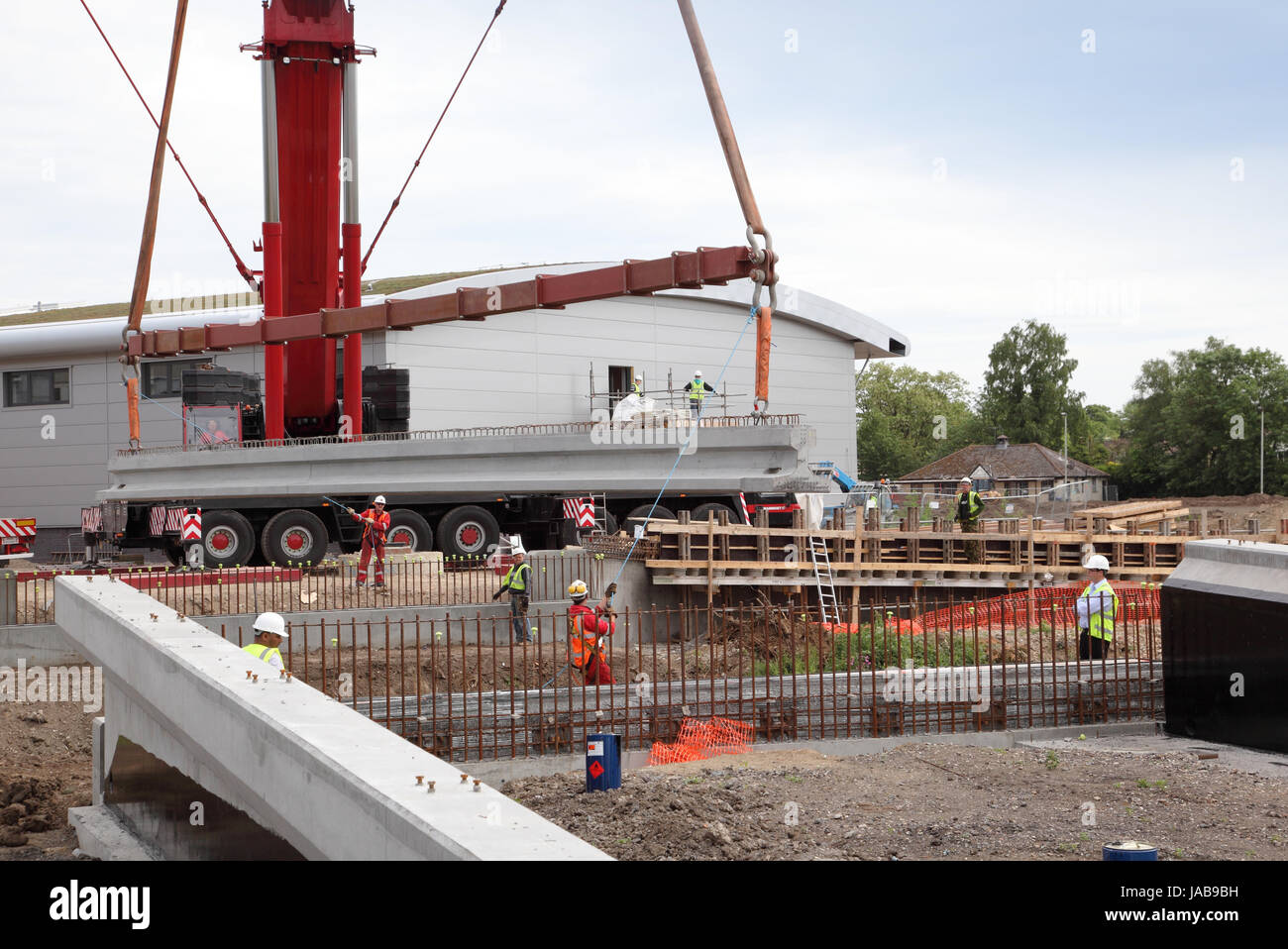 A mobile crane lifts a large, pre-cast concrete beam into place for the construction of a new road bridge in Woking, Surrey, UK Stock Photo