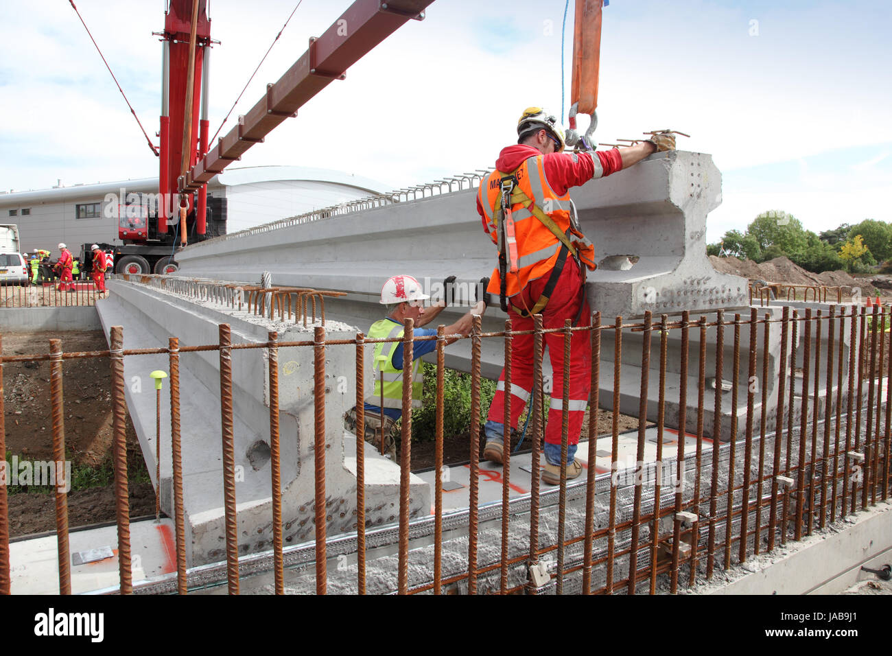 Workmen guide a large, pre-cast concrete beam into place for the construction of a new road bridge in Woking, Surrey, UK Stock Photo