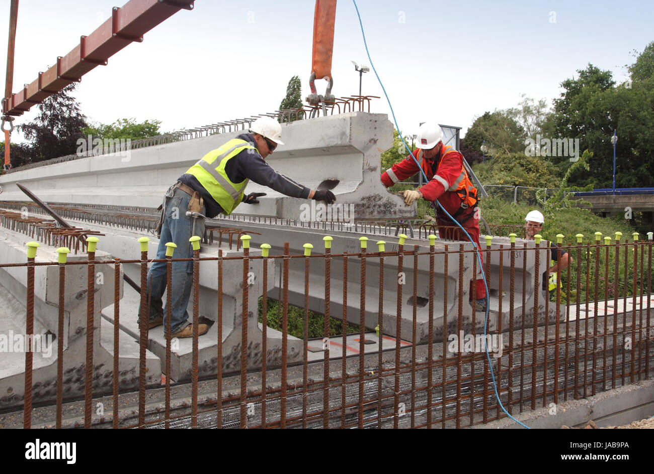 Workmen guide a large, pre-cast concrete beam into place for the construction of a new road bridge in Woking, Surrey, UK Stock Photo