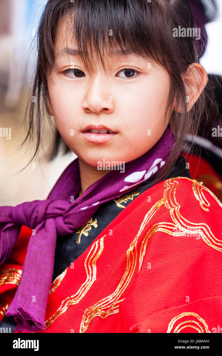 Japanese, Asian child, girl, 9-10 years old, head and shoulders. Wearing red yukata coat, aside view but head turned to face, eyes glancing around. Stock Photo