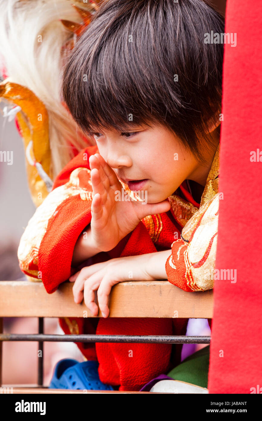 Japanese child, boy, 8-9 years old, leaning over wooden rail as he talks to someone (unseen) Hand cupped around mouth as if calling somone. Stock Photo