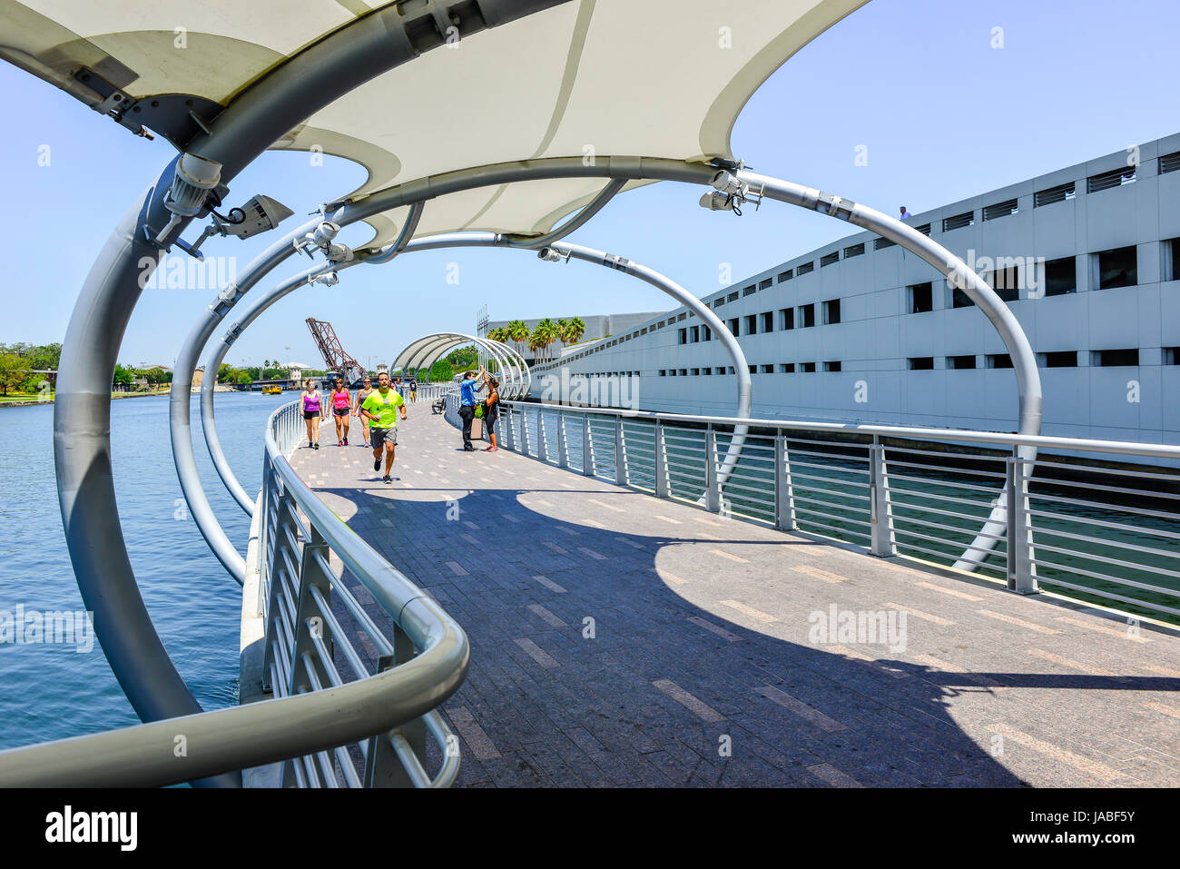 Pedestrians enjoy a stroll on the Tampa River Walk along the Hillsborough River with sunshade sails overhead with many nearby attractions in Tampa, FL Stock Photo