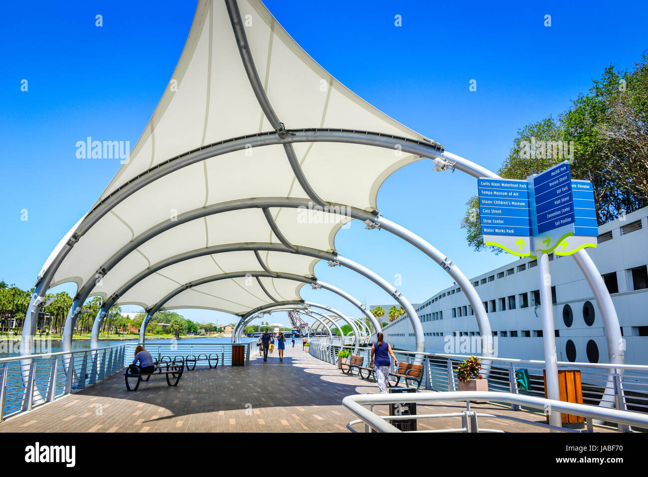 Pedestrians enjoy a stroll on the Tampa River Walk along the Hillsborough River with sunshade sails overhead with many nearby attractions in Tampa, FL Stock Photo