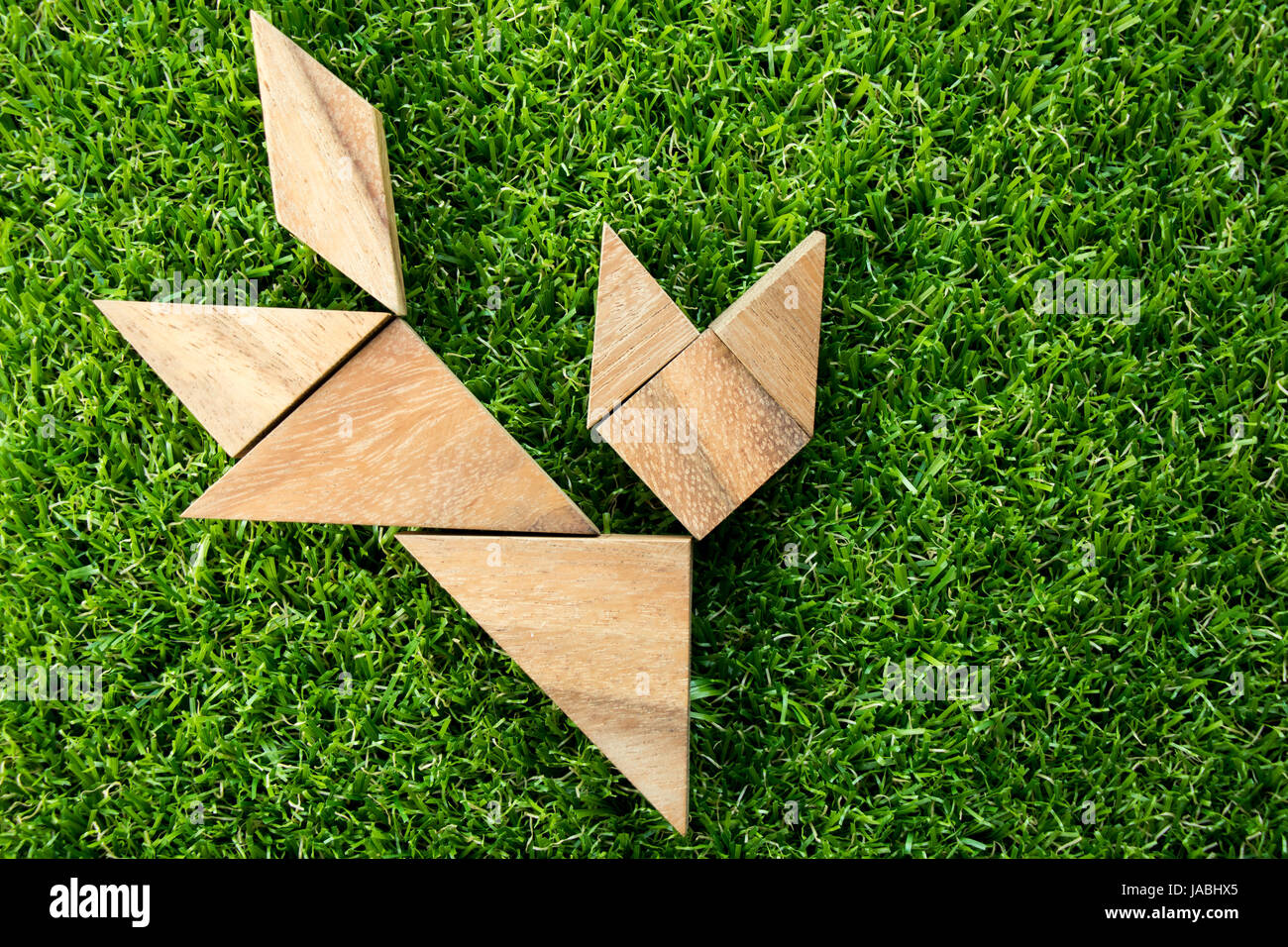 Wooden tangram puzzle in cat shape on artificial green grass background
