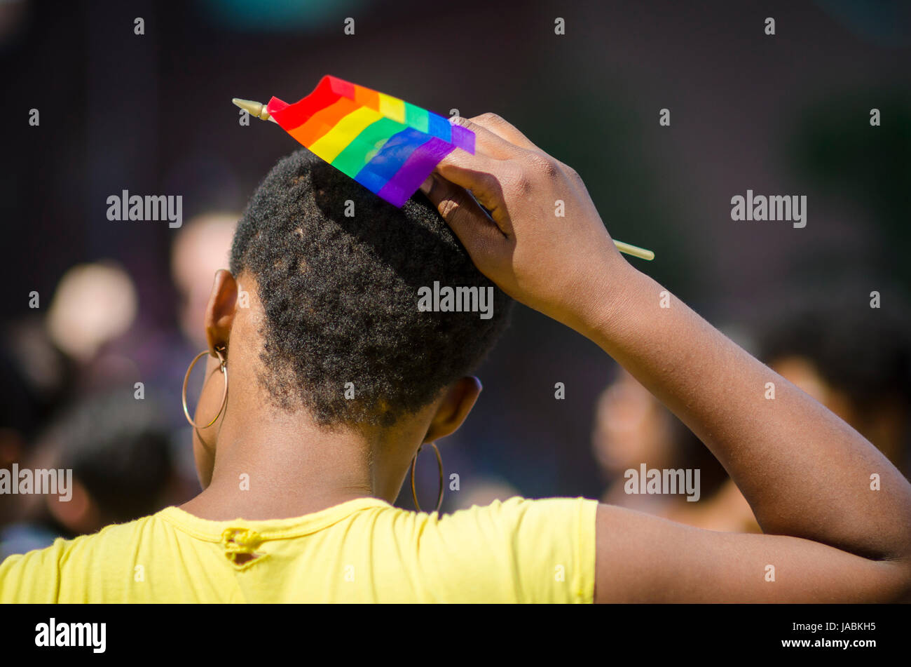 Unidentifiable african-american woman places rainbow flag in her afro hair on the sidelines of a summer gay pride parade Stock Photo