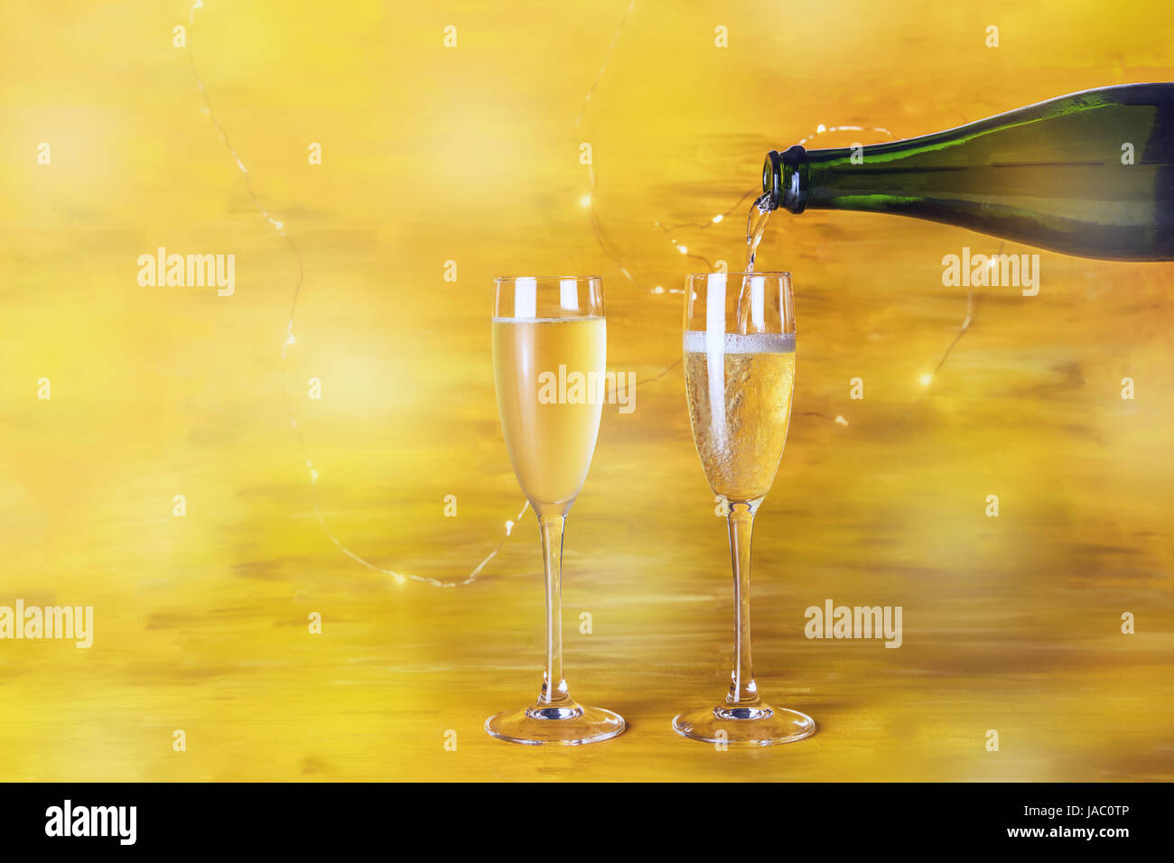 Champagne being poured into glasses on a blurred golden background with shining lights, with a place for text Stock Photo
