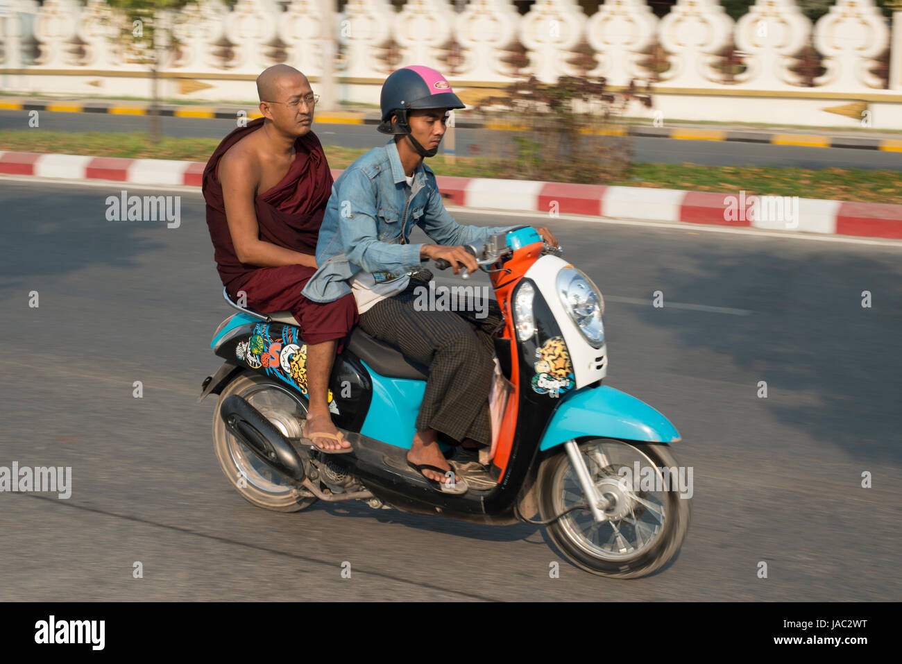 A Buddhist monk rides pillion on a motorbike in Mandalay, Myanmar (Burma) Stock Photo