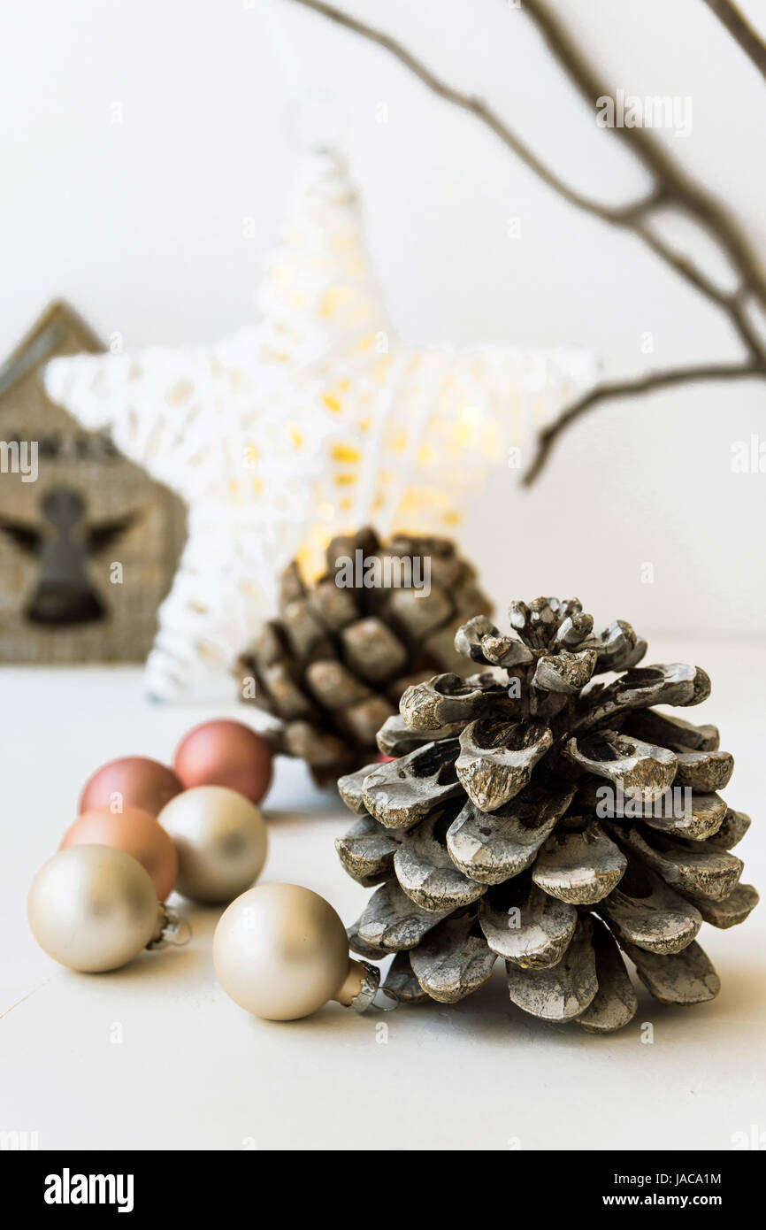 White Christmas decoration composition, big pine cones, scattered baubles, shiny star, wooden candle holder, dry tree branches in background, closeup Stock Photo