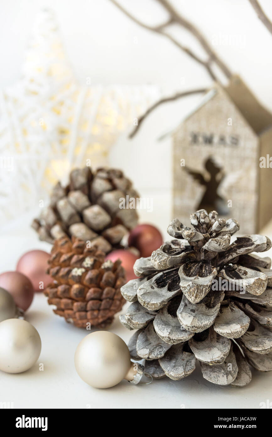 White Christmas decoration composition, big pine cones, scattered baubles, shiny star, wooden candle holder, dry tree branches in background, minimali Stock Photo