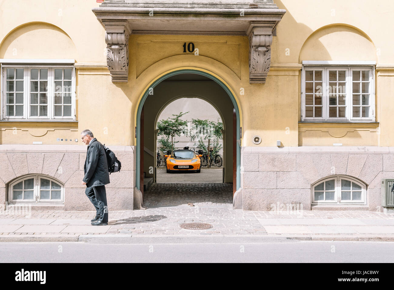 Copenhagen, Denmark - August 10, 2016. Unidentified middle aged man walking at the door entrance to a house with a luxury sport car parked in the pati Stock Photo