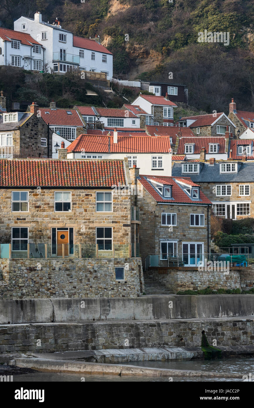 Scenic view of pretty quaint coastal village & seaside houses huddled on the cliff side above the harbour wall - Runswick Bay, Yorkshire, England, UK. Stock Photo
