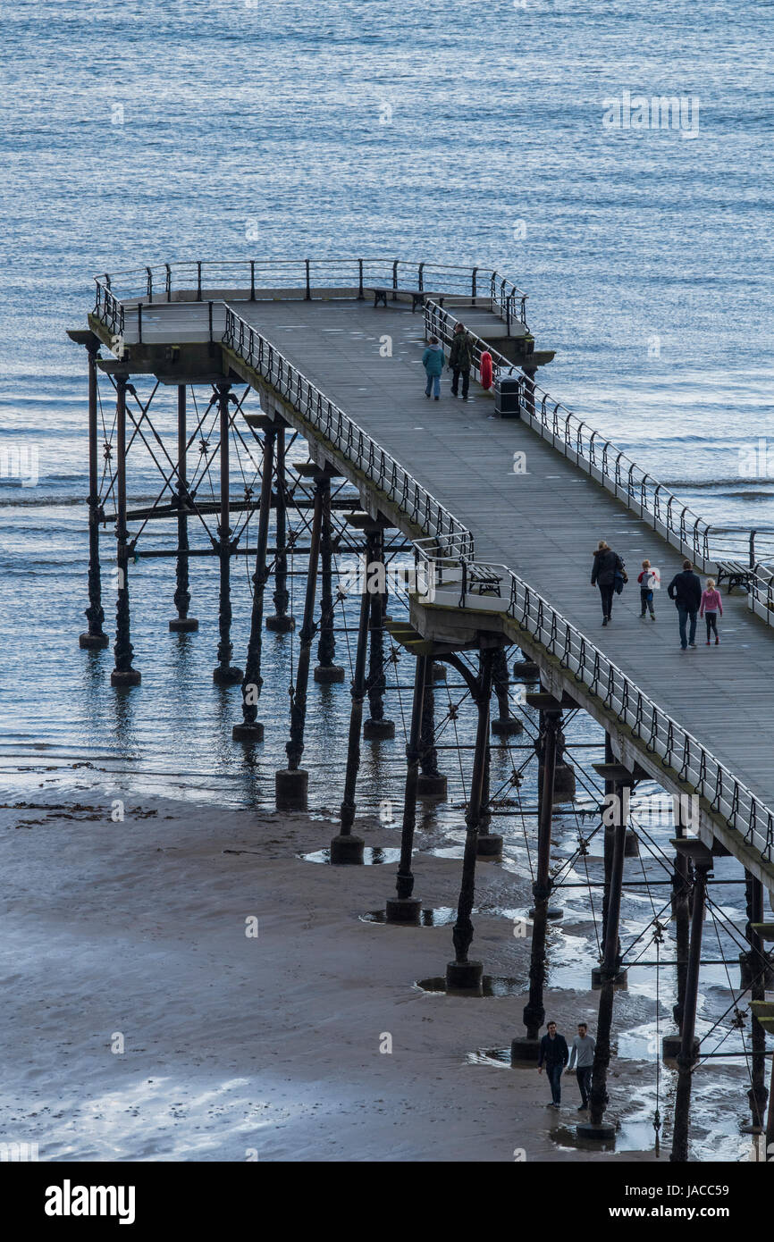 High view of people on Victorian pleasure pier, jutting out into North Sea on grey spring day - Saltburn-by-the-Sea, North Yorkshire, England, GB, UK. Stock Photo