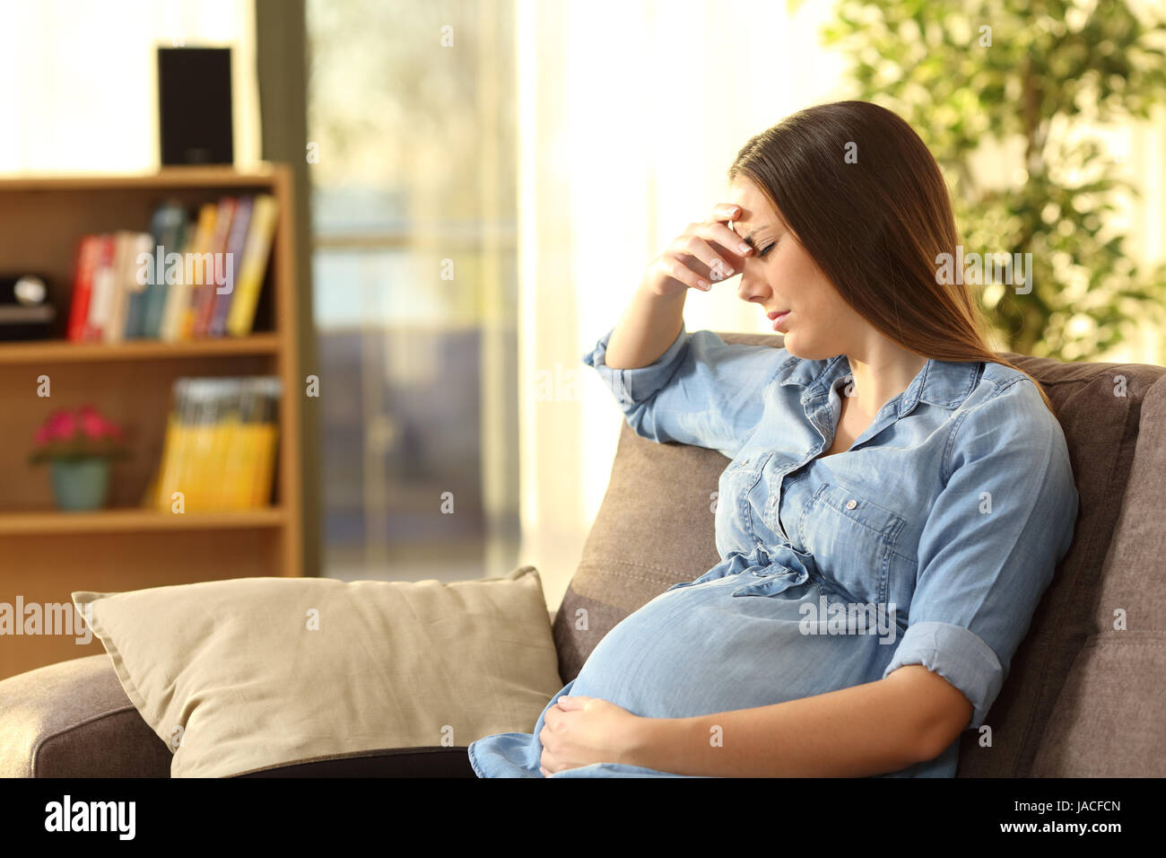 Worried pregnant woman sitting on a couch in the living room at home Stock Photo