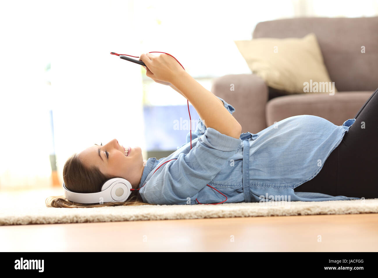 Side view of a pregnant woman listening music with headphones and a smart phone lying on the floor at home Stock Photo