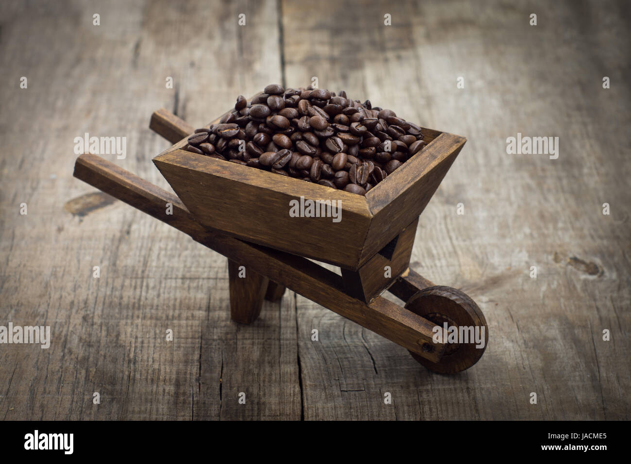 A wheelbarrow full of coffee beans on wood background Stock Photo