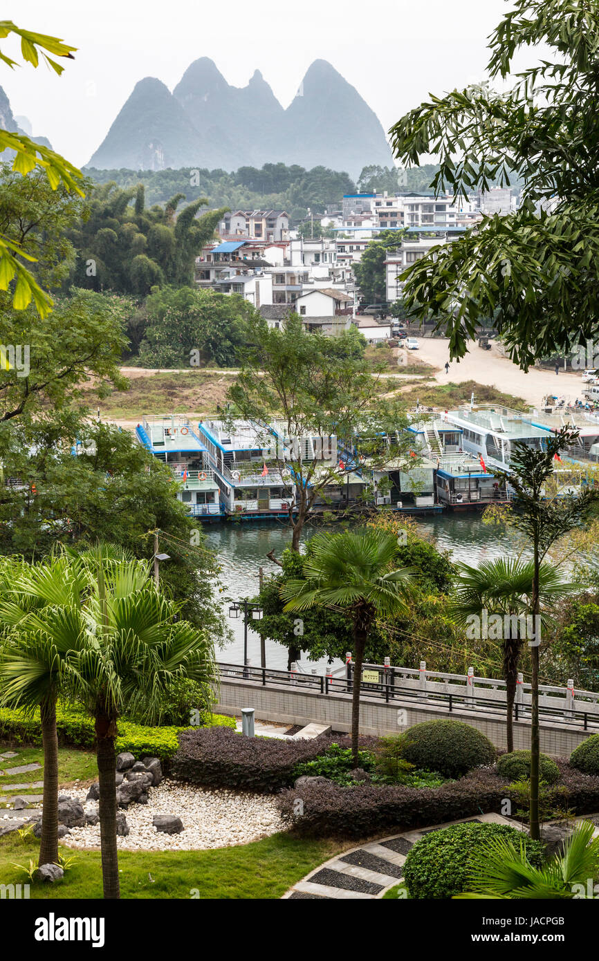 Yangshuo, China.  View from Hotel Window.  River Cruise Boats in foreground, City Houses in Mid-ground, Karst Landscape in Background. Stock Photo