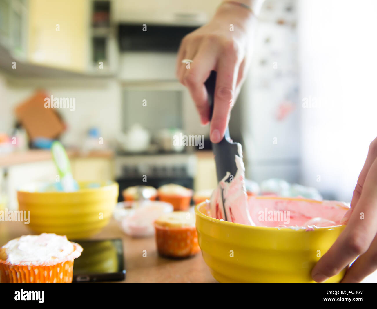 Close shot of many sweet cupcakes on the foreground while a baker decorating the last one Stock Photo