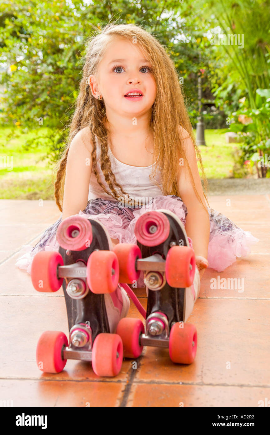 Little girl preschool sitting on ground wearing her roller skates, in a