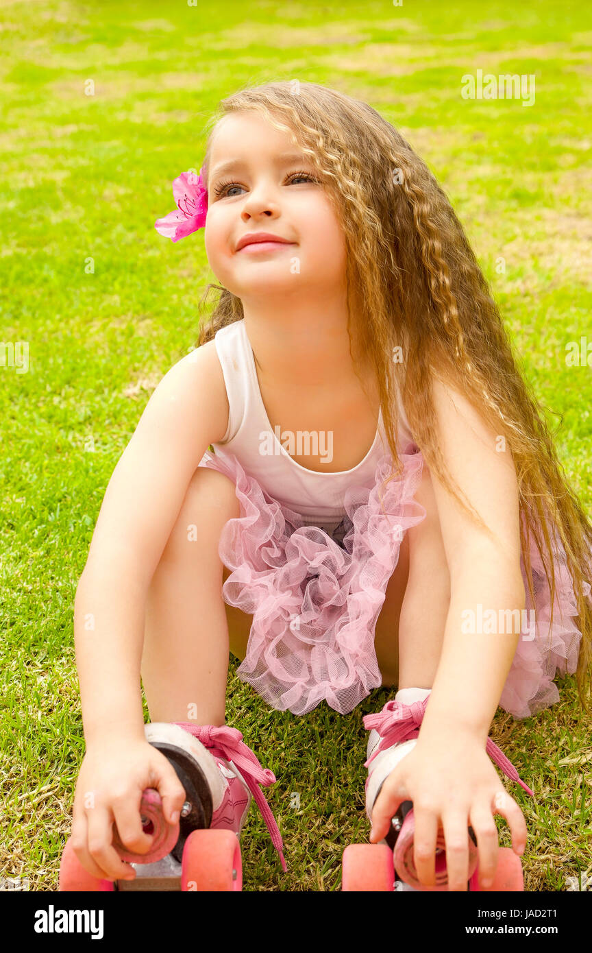 Little girl preschool beginner sitting in the grass with her roller skates, in a grass background Stock Photo