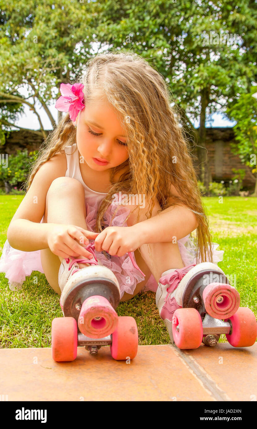 Little girl preschool beginner tie the laces of her roller skates, in a  grass background Stock Photo - Alamy