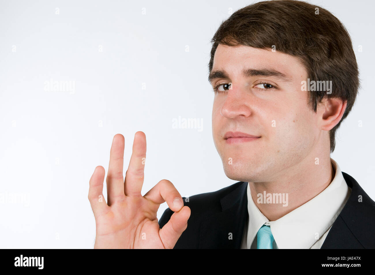 Kopf-und-Schulter-Portärt eines jungen Mannes in schwarzen Anzug vor weißen Hintergrund das O.K.-Zeichen in die Kamera zeigend Stock Photo