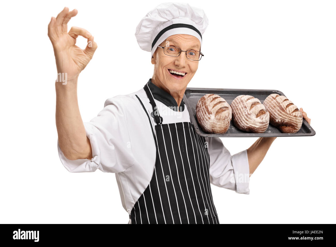 Joyful mature baker holding a tray with loaves of bread and making an ok sign isolated on white background Stock Photo