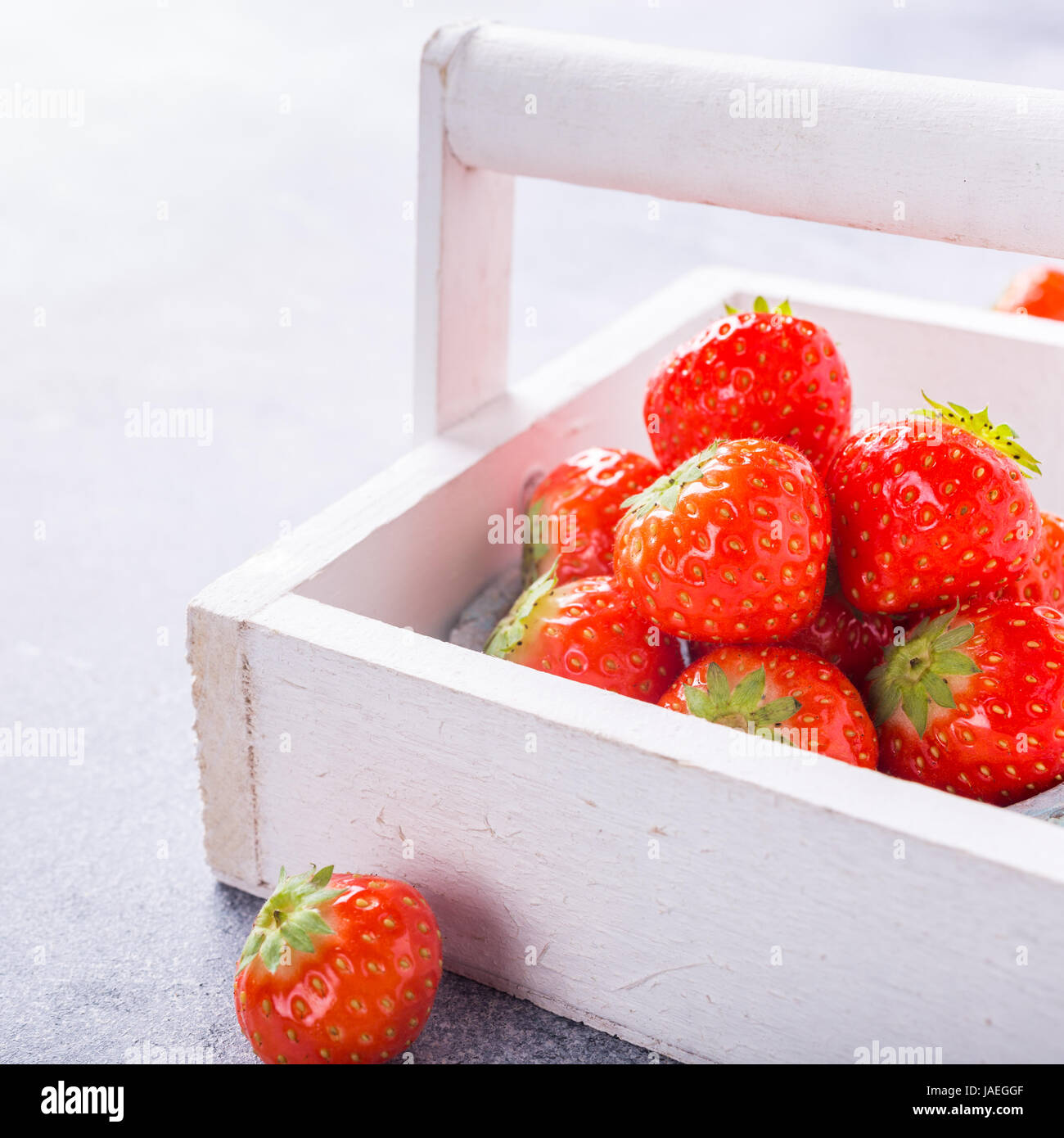 White wooden box filled with succulent juicy fresh ripe red strawberries on gray stone table top. Healthy food. Copy space. Stock Photo