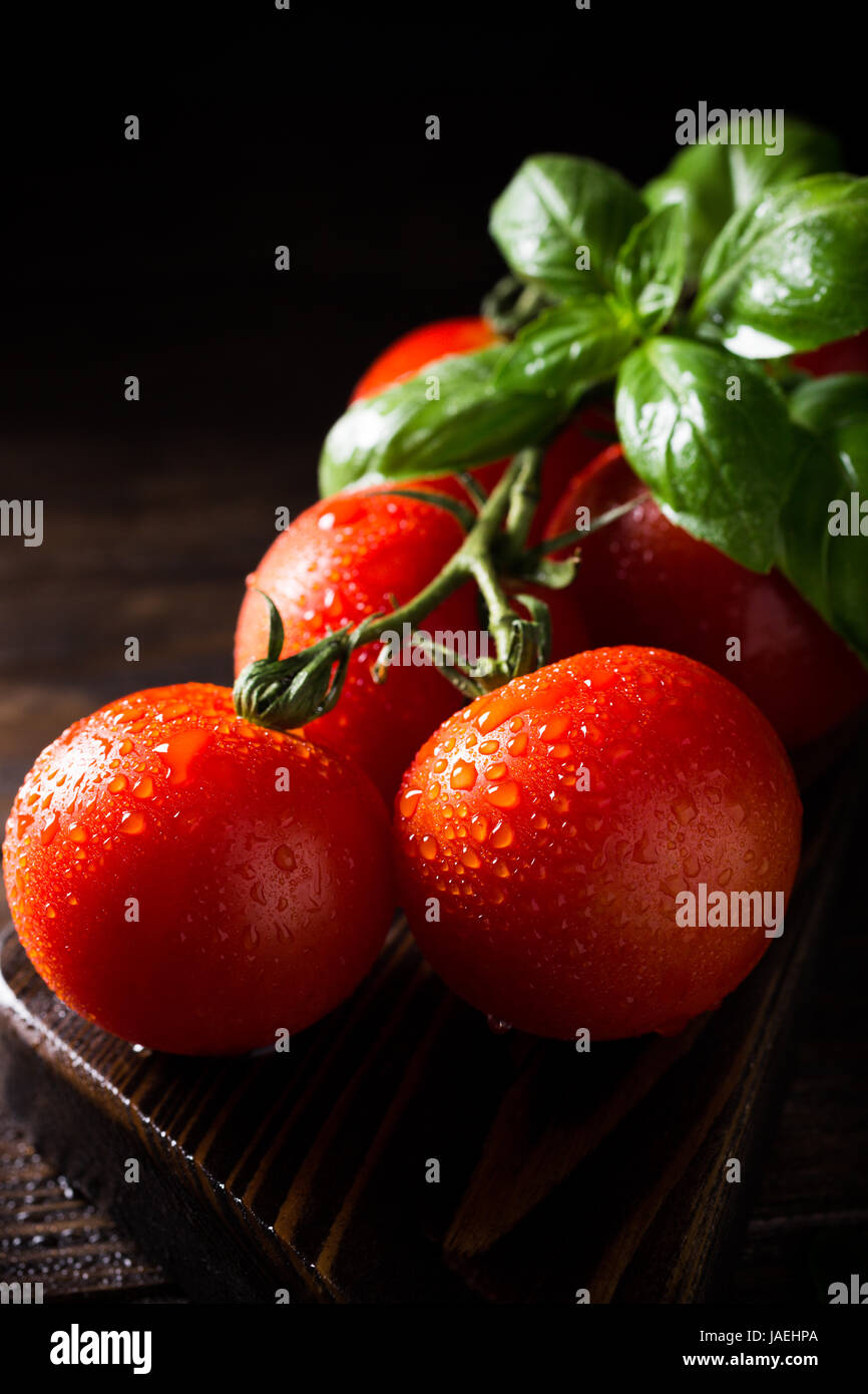 Branch of ripe natural tomatoes and basil leaves on wooden cutting ...