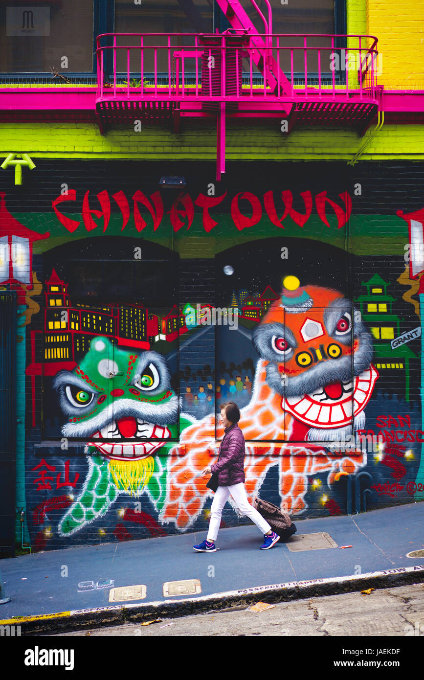 A woman walking down a downward alley past a wall of graffiti portraying Chinese dragon dancing in Chinatown in San Francisco, California Stock Photo