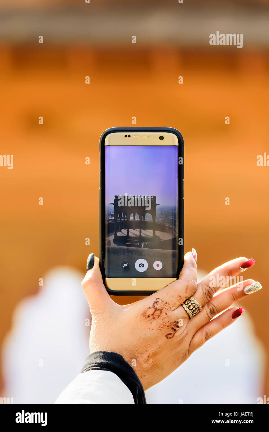 Closeup of a woman hand holding a smartphone taking photo of a dome in a fort in Rajasthan, India Stock Photo