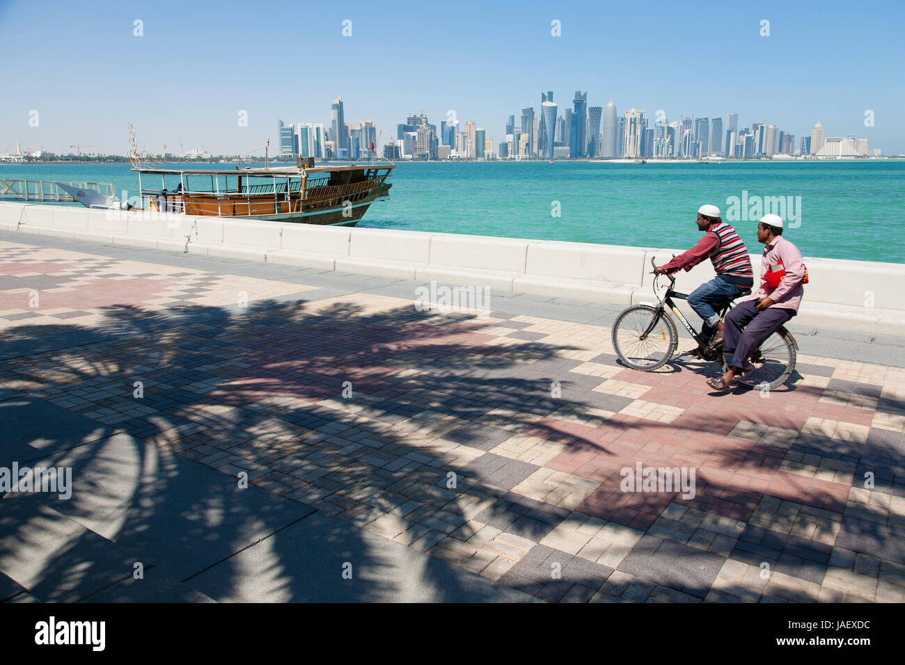 A cyclist with passenger pedals along the Corniche Promenade, Doha, Qatar, looking towards West Bay Stock Photo