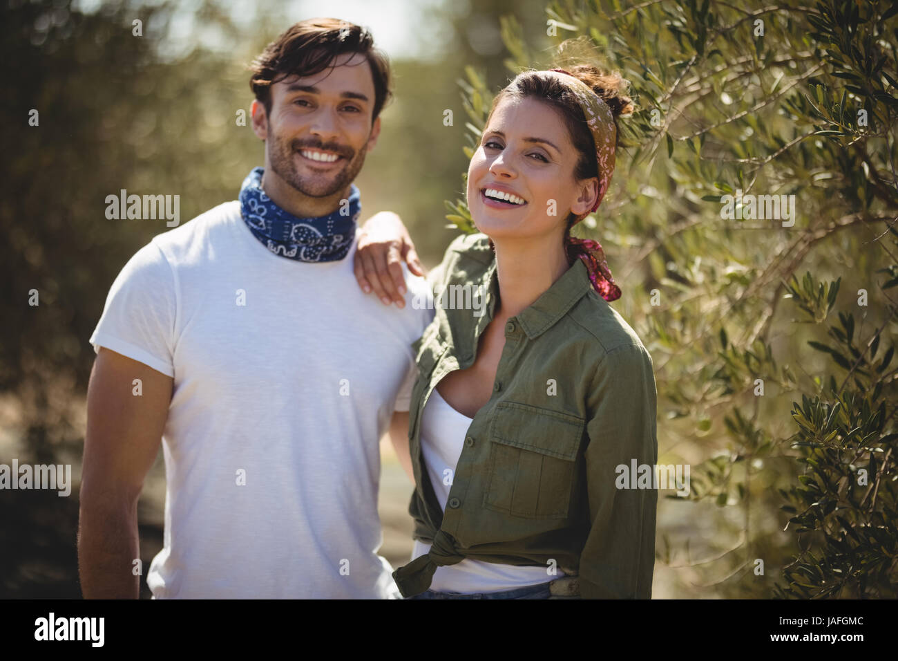 Portrait of cheerful young couple standing by trees at farm Stock Photo ...