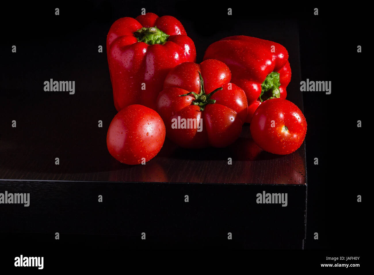 Three big jucy bell peppers and fresh tomatoes on dark wooden background Stock Photo