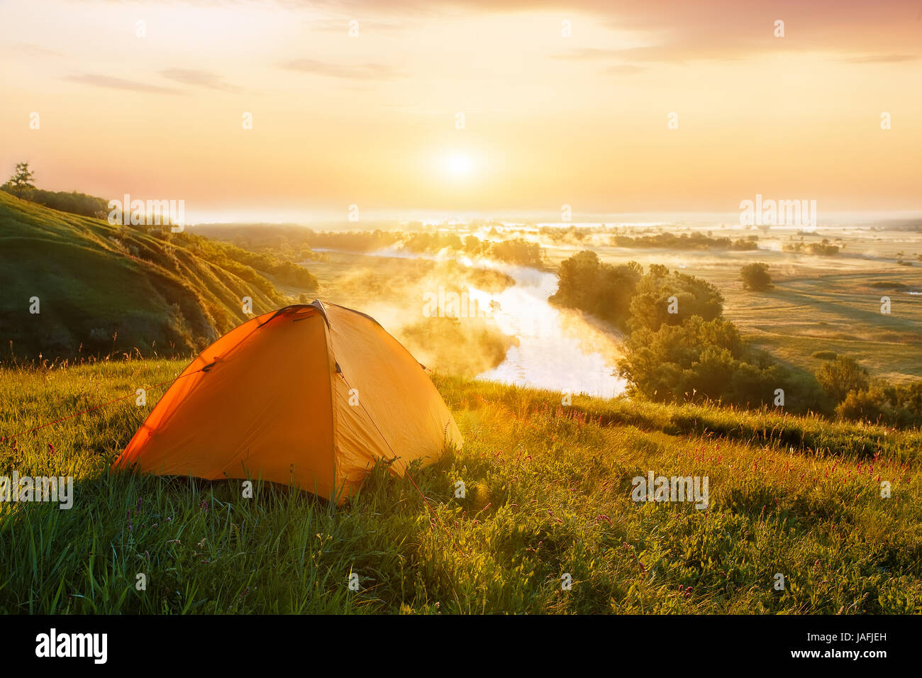 view of tourist tent on green meadow at sunrise or sunset. Camping ...