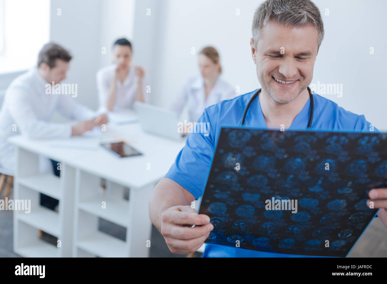 Examining positive mrt result . Confident attentive optimistic neurologist working at the hospital and examining mrt scan results while colleagues sha Stock Photo