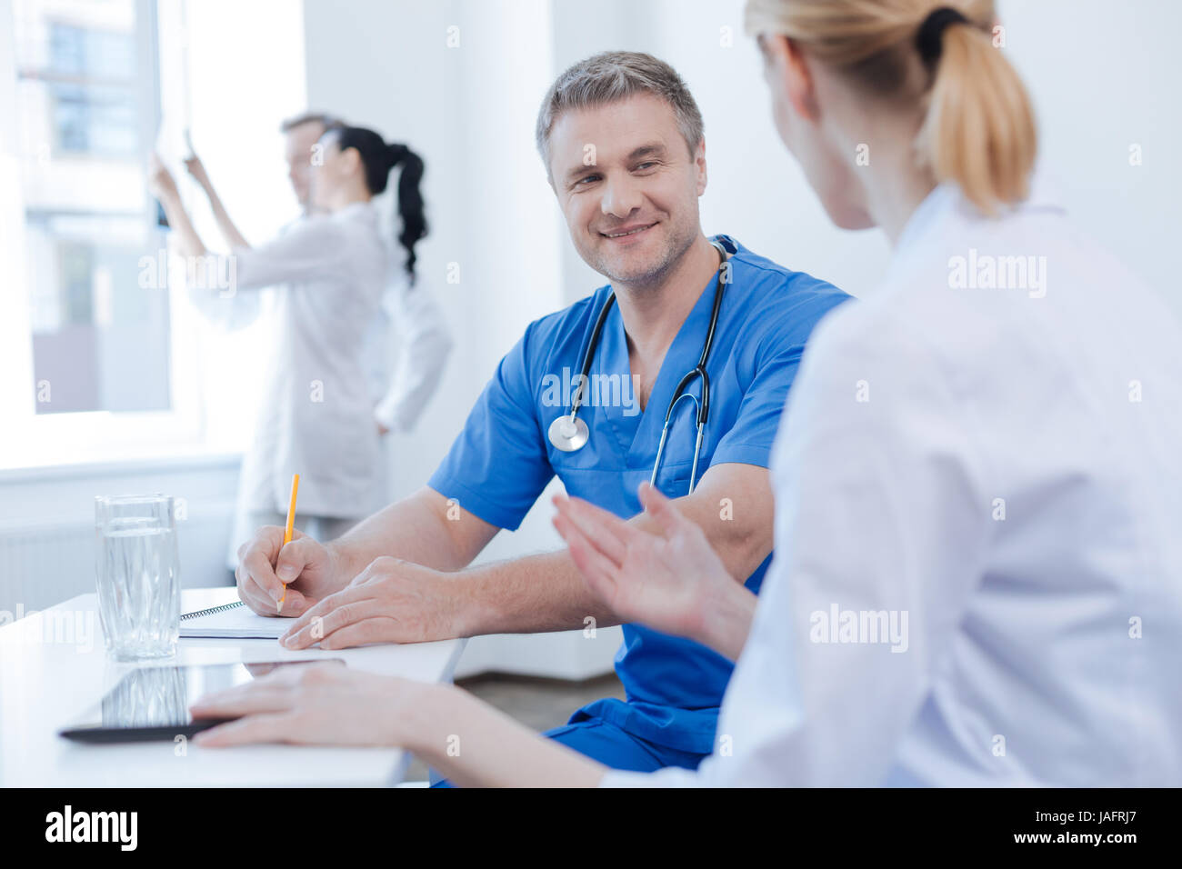 Sharing our professionalism. Cheerful delighted qualified medics working and sharing professional experience in the hospital while using digital table Stock Photo