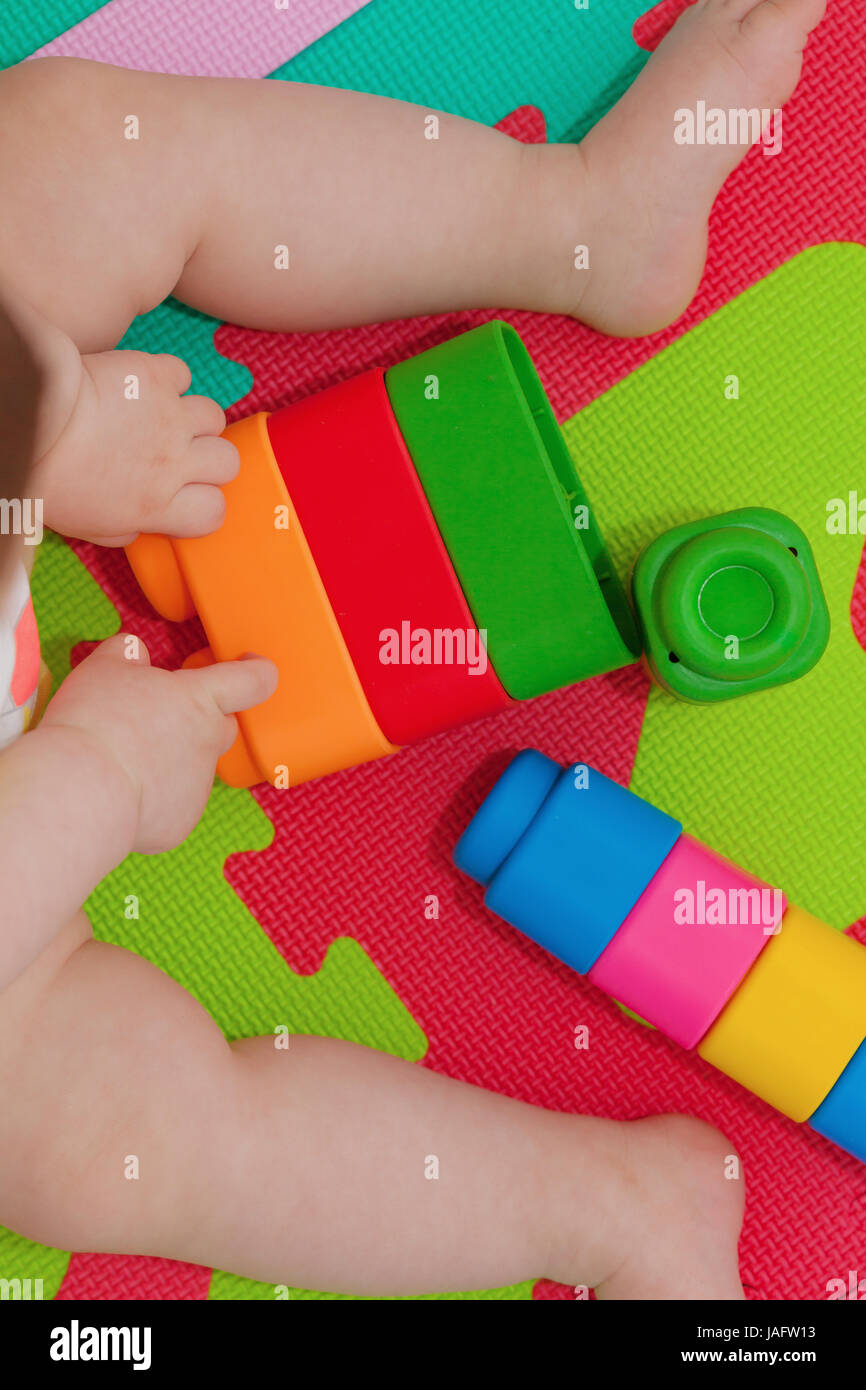 Toddler plays with building block on the colored rubber mat. Stock Photo