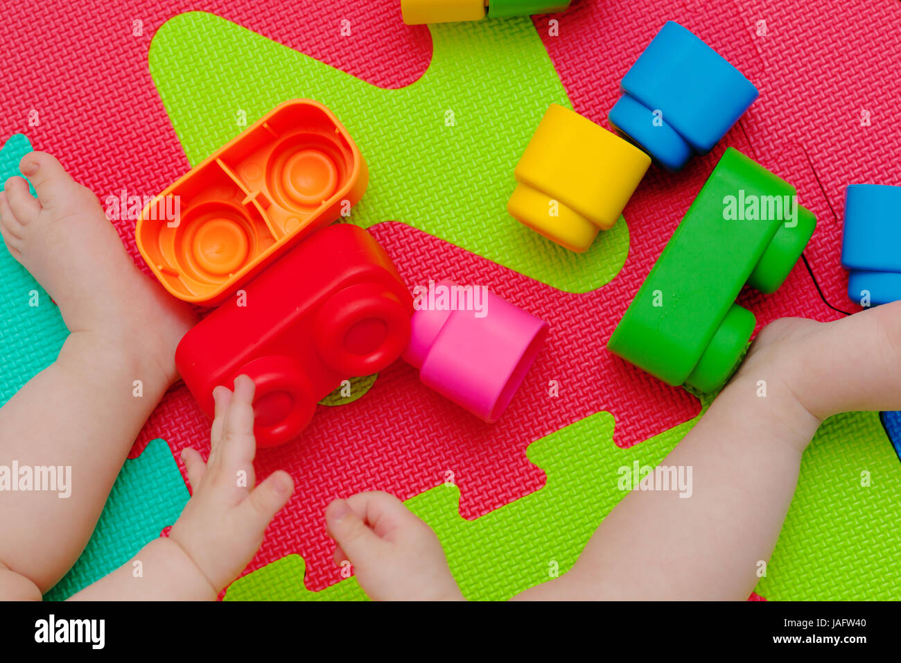Toddler plays with building block on the colored rubber mat. Stock Photo