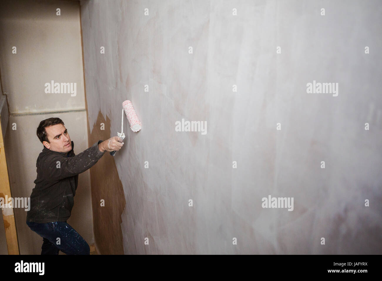 A builder, a painter holding a paint roll, painting a wall with white